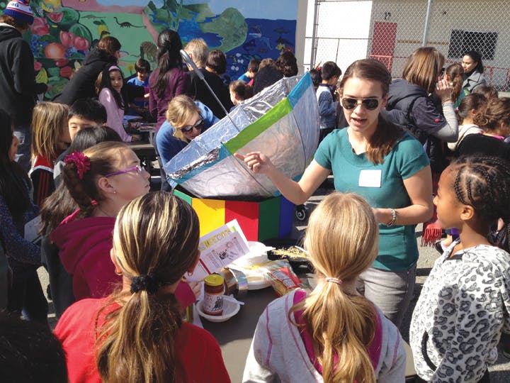 A Cal Poly Pomona student helps children at Santa Monicas McKinley Elementary School work a solar cooker, developed with HMC vo
