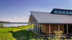 university building sitting beneath blue sky with large body of water behind it with green grass to its left university building sitting beneath blue sky with large body of water behind it with green grass to its left