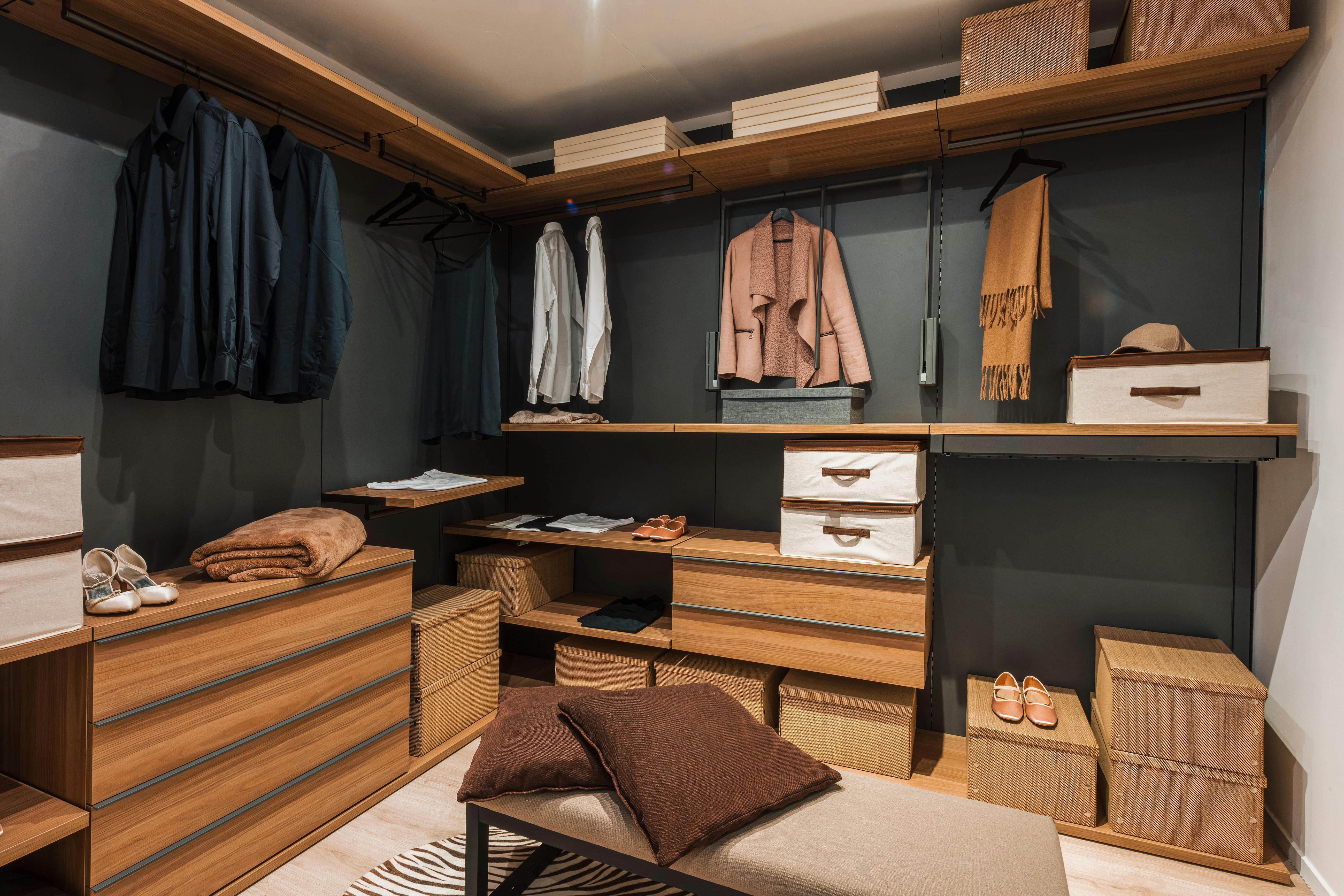 Modern walk in closet showing organized clothes, shoes, and accessories. Interior of a modern and spacious walk in closet featuring wooden shelves, drawers, and organized clothing, shoes, and accessories