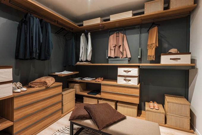 Modern walk in closet showing organized clothes, shoes, and accessories. Interior of a modern and spacious walk in closet featuring wooden shelves, drawers, and organized clothing, shoes, and accessories