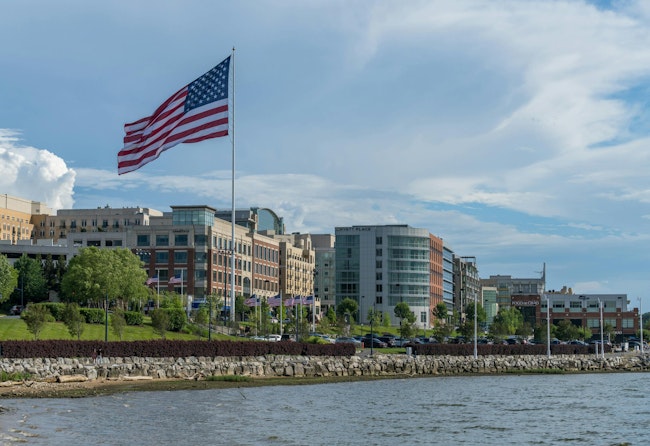 USA Flag flying at National Harbor in Maryland near Washington DC. National Harbor, MD - 24 June 2023: Skyline of National Harbor with large USA Flag flying near Washington DC