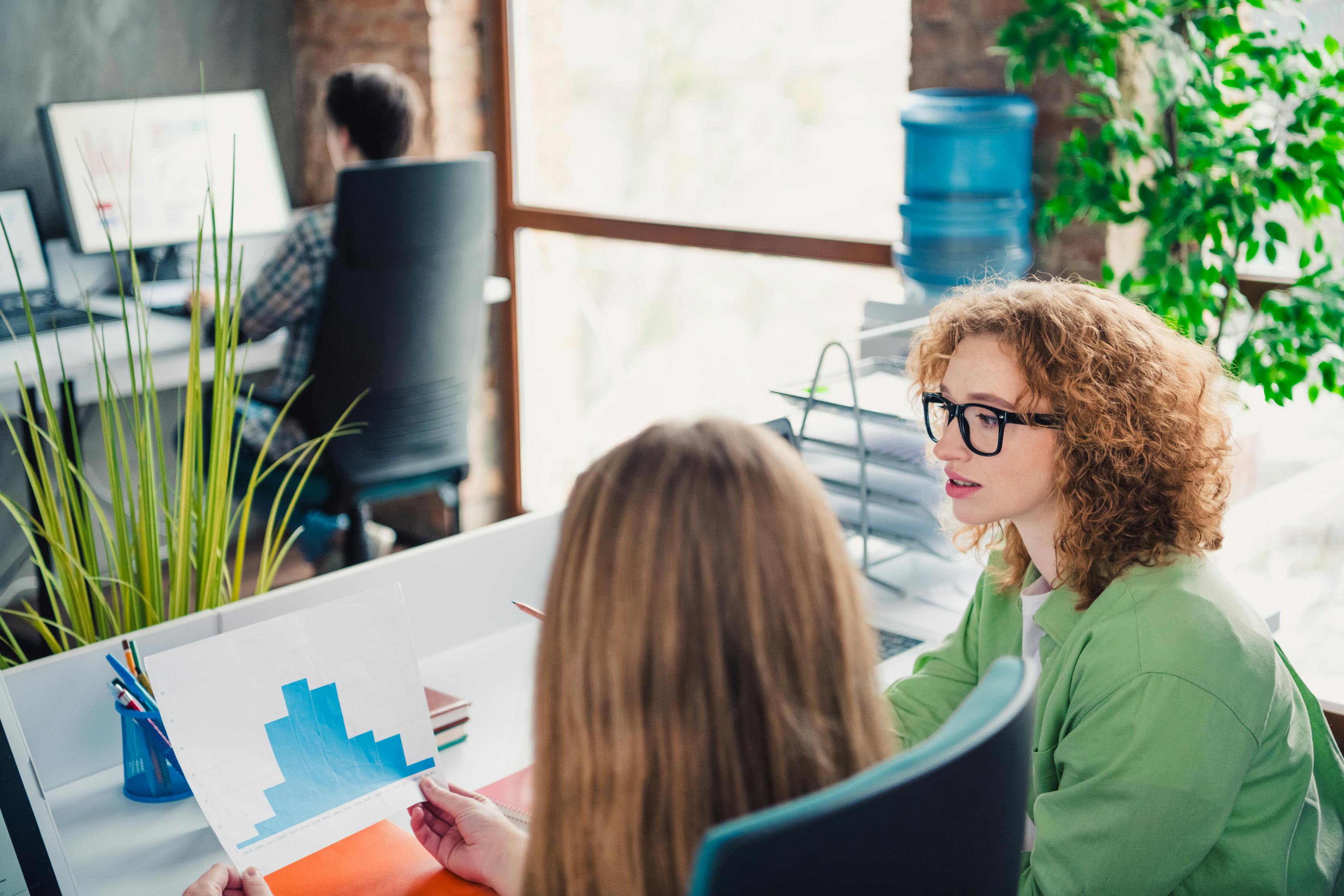 Young professionals discussing workplace strategies at a modern open office, fostering collaboration, teamwork. A diverse group of young professionals collaborating in an open office environment. They are sharing ideas, analyzing documents, and supporting teamwork to achieve goals within a creative and friendly workplace setting.
