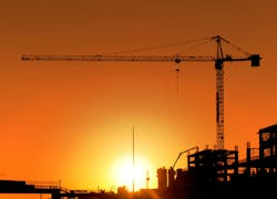 Construction Site and Crane. Horizontal photo of a construction site including a crane at sunset. The area is totally orange colored and all the buildings and equipment is seen as a silhouette Construction Site and Crane. Horizontal photo of a construction site including a crane at sunset. The area is totally orange colored and all the buildings and equipment is seen as a silhouette