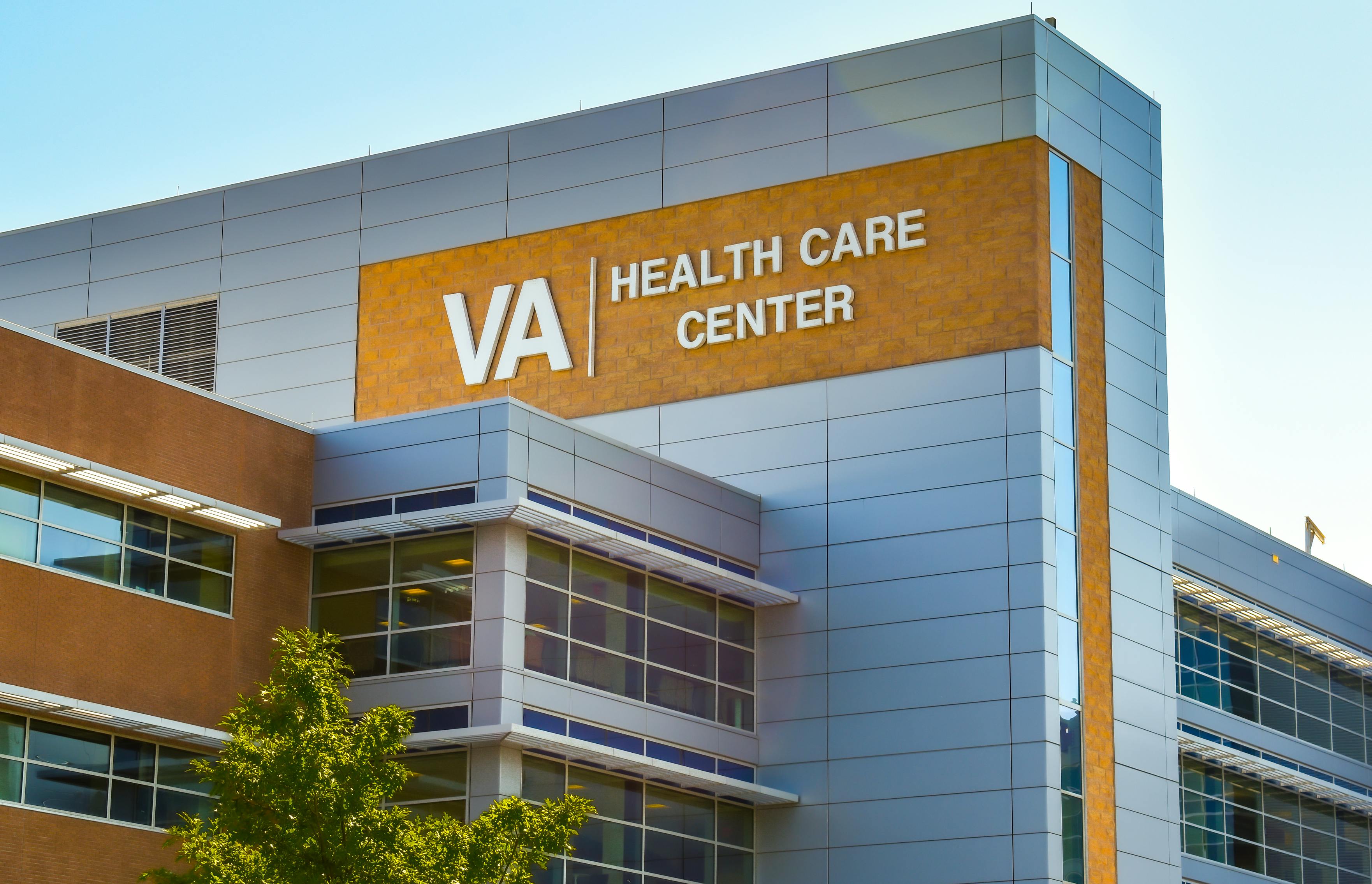 Veterans Administration Health Care Center. Horizontal, medium closeup of VA Health Care Center medical facilities exterior facade brand and logo signage adorning the modern architecture of the building in Charlotte, North Carolina with floors of reflective windows and a clear blue sky in the soft light of early morning.