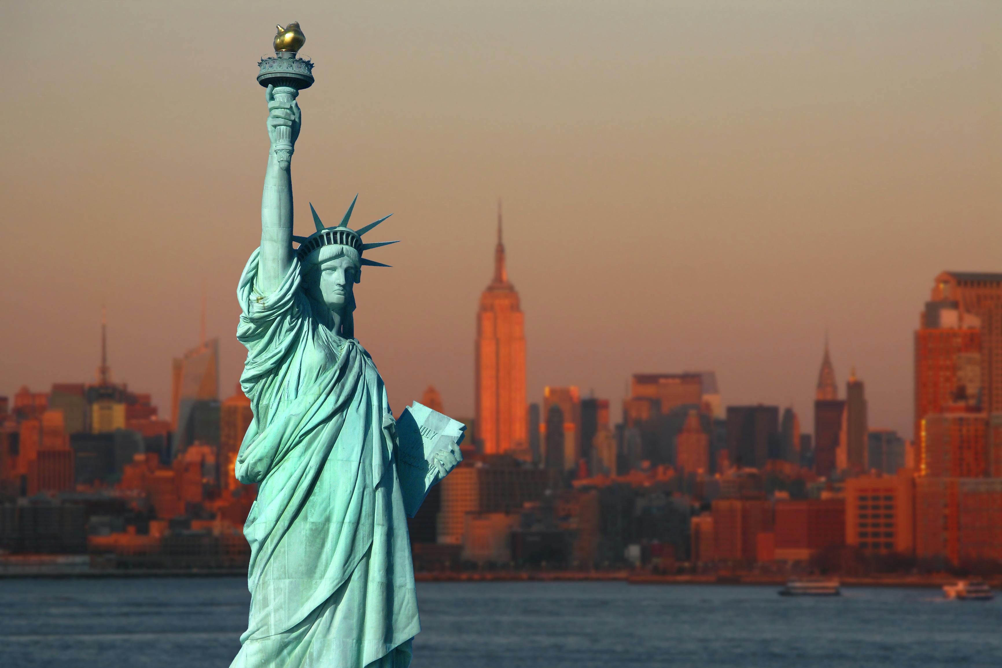 New York: The Statue of Liberty, an American symbol, with Lower Manhattan skyline at sunset in the background. Tourism concept photo. Liberty Island, New York City, USA