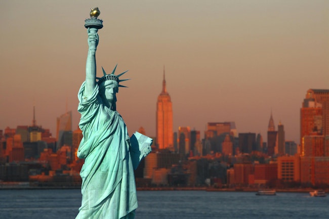 New York: The Statue of Liberty, an American symbol, with Lower Manhattan skyline at sunset in the background. Tourism concept photo. Liberty Island, New York City, USA