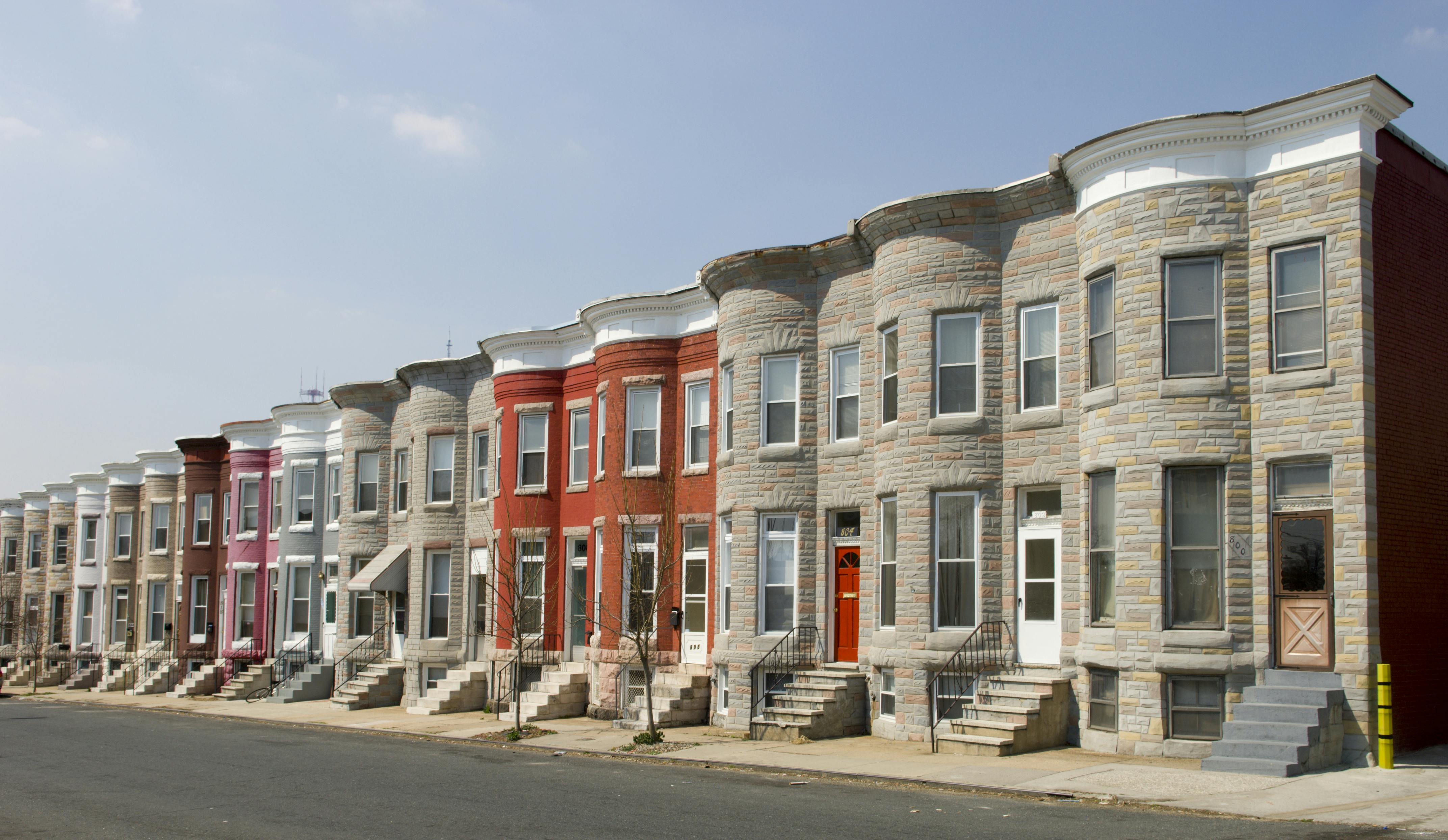 Colorful row houses along a residential street in Baltimore with painted brick and formstone facades and marble stoops.