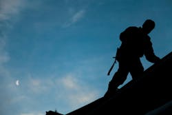 Contractor in Silhouette working on a Roof Top with blue Sky in Background Contractor in Silhouette working on a Roof Top with blue Sky in Background