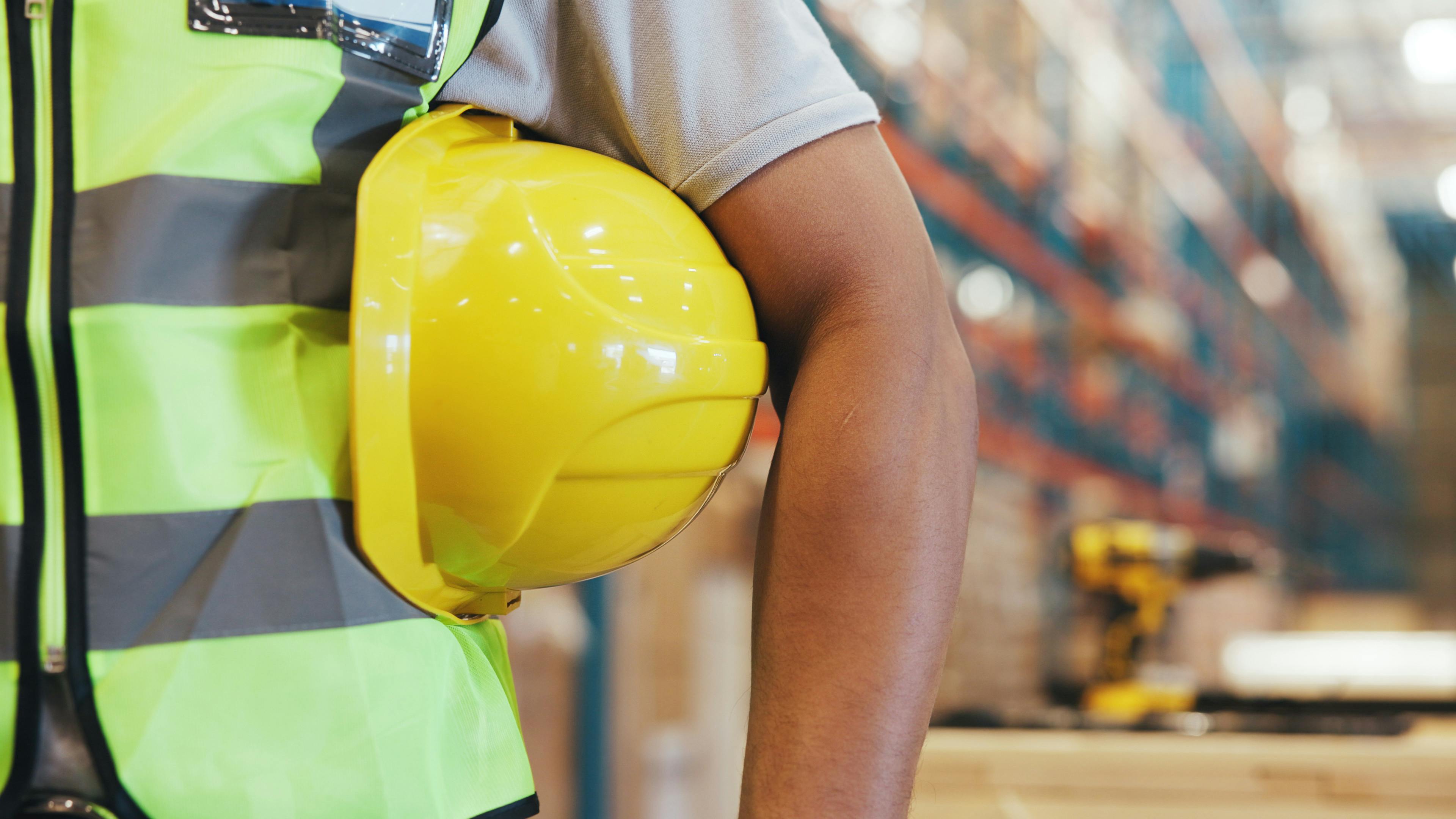 Helmet, logistics and arm of man in warehouse for safety manager, contractor and packing technician. Supply chain, ppe protection and hardhat gear with person in factory for distribution and bokeh.