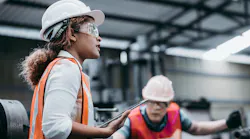 Female industrial engineer wearing a white helmet while standing in a heavy industrial factory behind she talking with workers, Various metal parts of the project