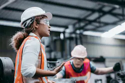 Female industrial engineer wearing a white helmet while standing in a heavy industrial factory behind she talking with workers, Various metal parts of the project Female industrial engineer wearing a white helmet while standing in a heavy industrial factory behind she talking with workers, Various metal parts of the project