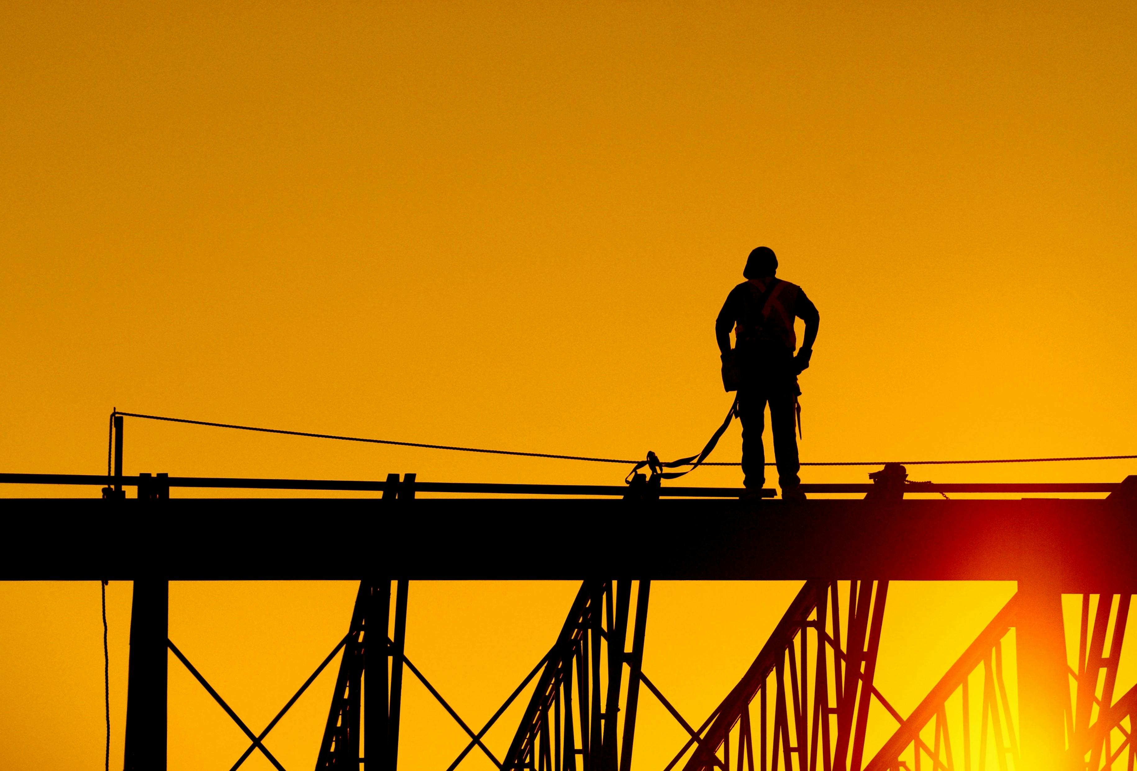 Construction worker stands on steel beam of building at sunrise.