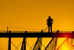 Construction worker stands on steel beam of building at sunrise.